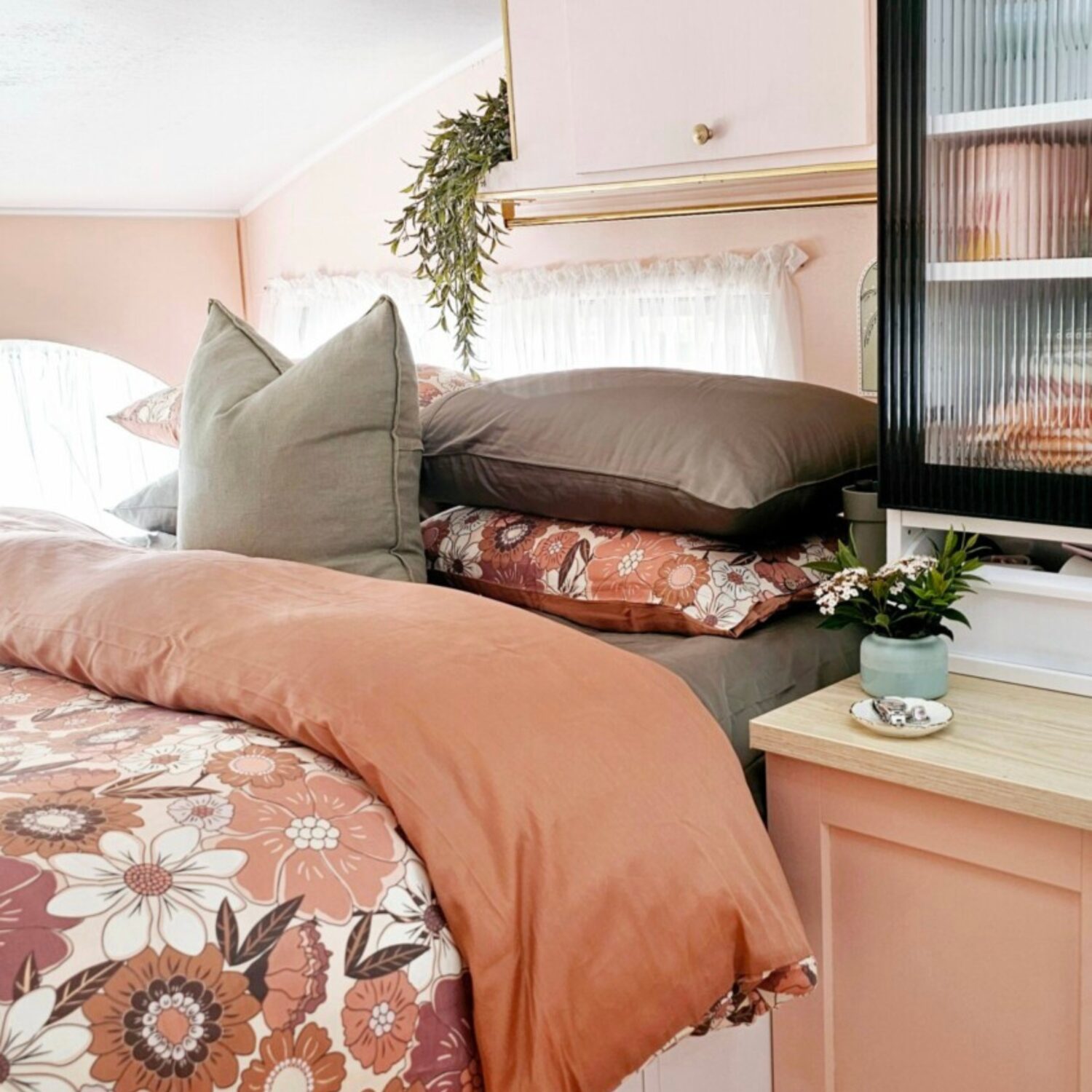 Pink caravan bed dressed in vintage floral and dusty rose Ecoluxe quilt covers, with sage pillows and morning light through the window