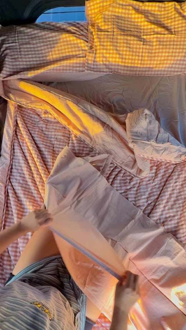 Pink-and-cream gingham bedding bathed in warm first light through a caravan window