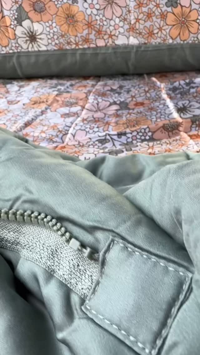 A close-up of the sage Zipluxe zipper joining two panels of bamboo bedding, with vintage florals beside