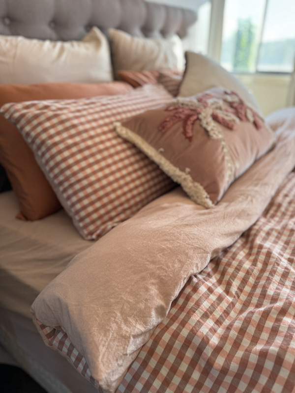 Terracotta gingham bedding stacked with a cream palm-tufted pillow and rust pillow case at home