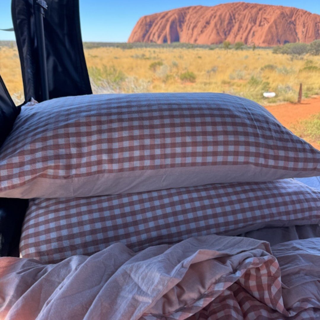 Brown gingham pillows stacked in a caravan with Uluru in the distance