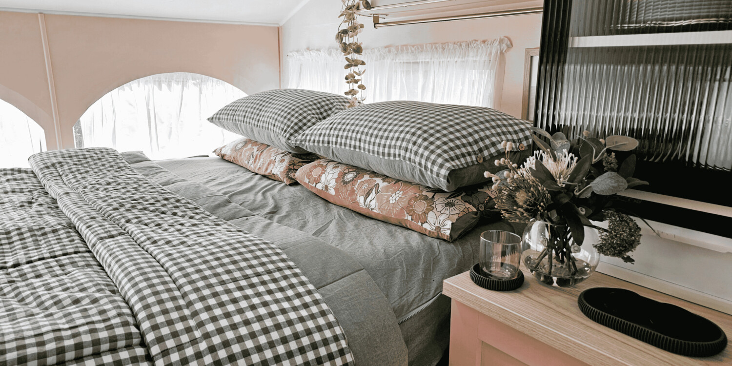 Pink caravan interior dressed in charcoal gingham bedding with a terracotta vintage-floral pillow and dried eucalyptus